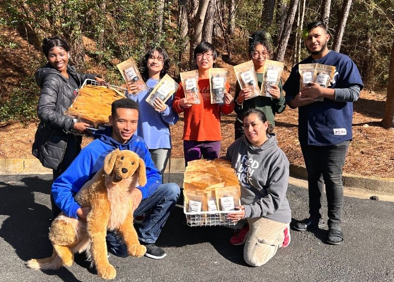 seven adults holding bagged treats and a stuffed puppy dog mascot