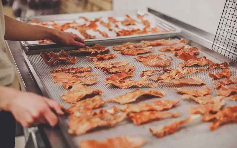 hands lifting a tray full of freshly dehydrated jerky