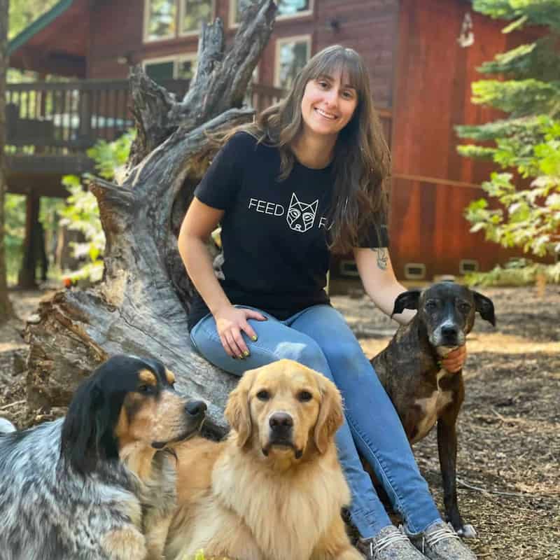 Woman sitting with three dogs in a rustic outdoor setting