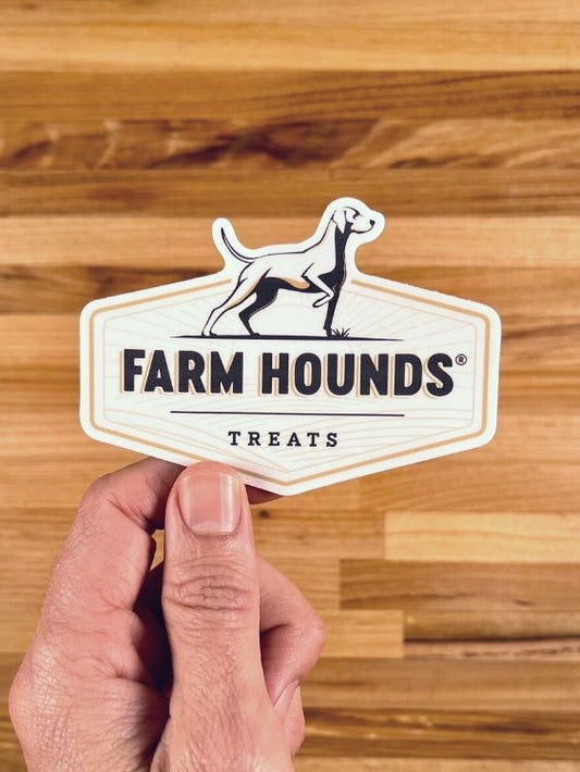 hand holding a farm hounds logo sticker in front of a butcher block countertop